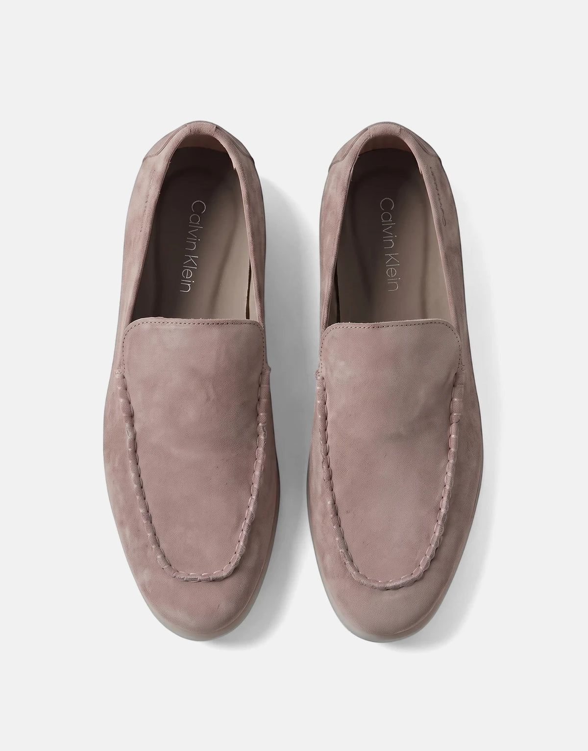 A pair of Calvin Klein Low Prof taupe suede loafers, seen from a top-down perspective, highlighting the moc-toe stitching.