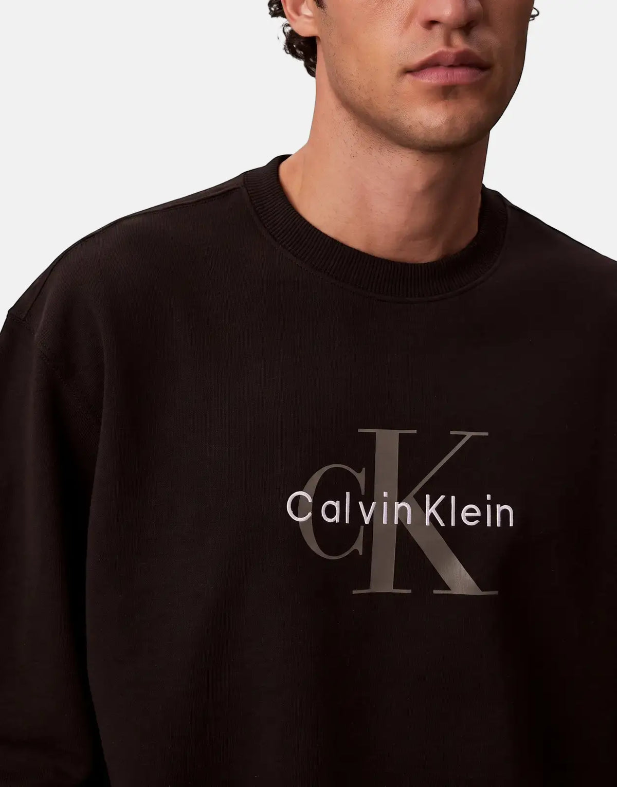Close-up of a man wearing a black Calvin Klein ML sweatshirt with a ribbed crew neck and iconic logo.