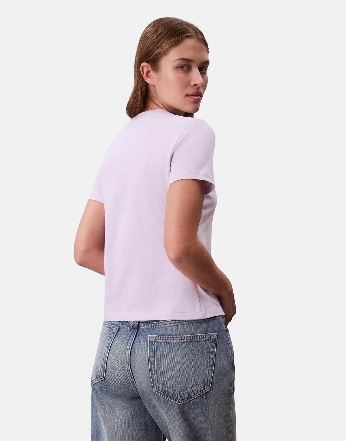 Woman wearing a Calvin Klein Seasonal Graphic Slim Lilac T-Shirt with blue jeans, depicted from the back looking over her