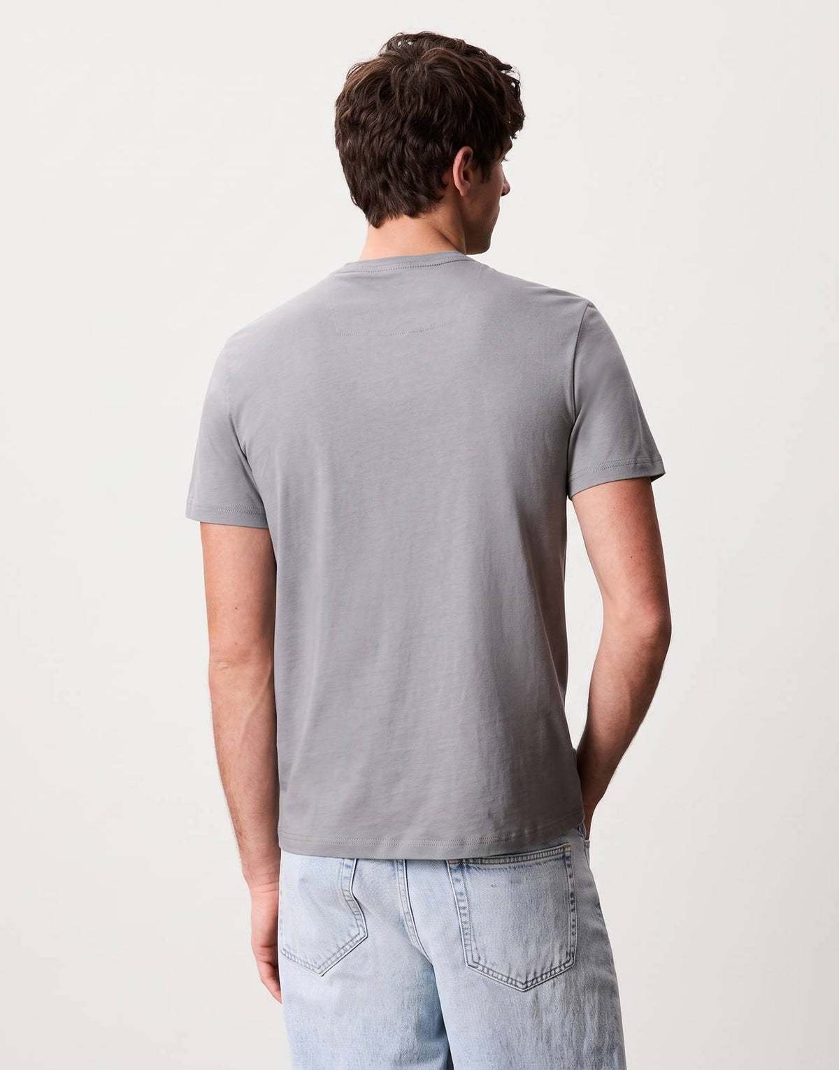 Calvin Klein Word Stack Graphic grey t-shirt, back view on a male model wearing light wash loose-fit jeans. Simple and