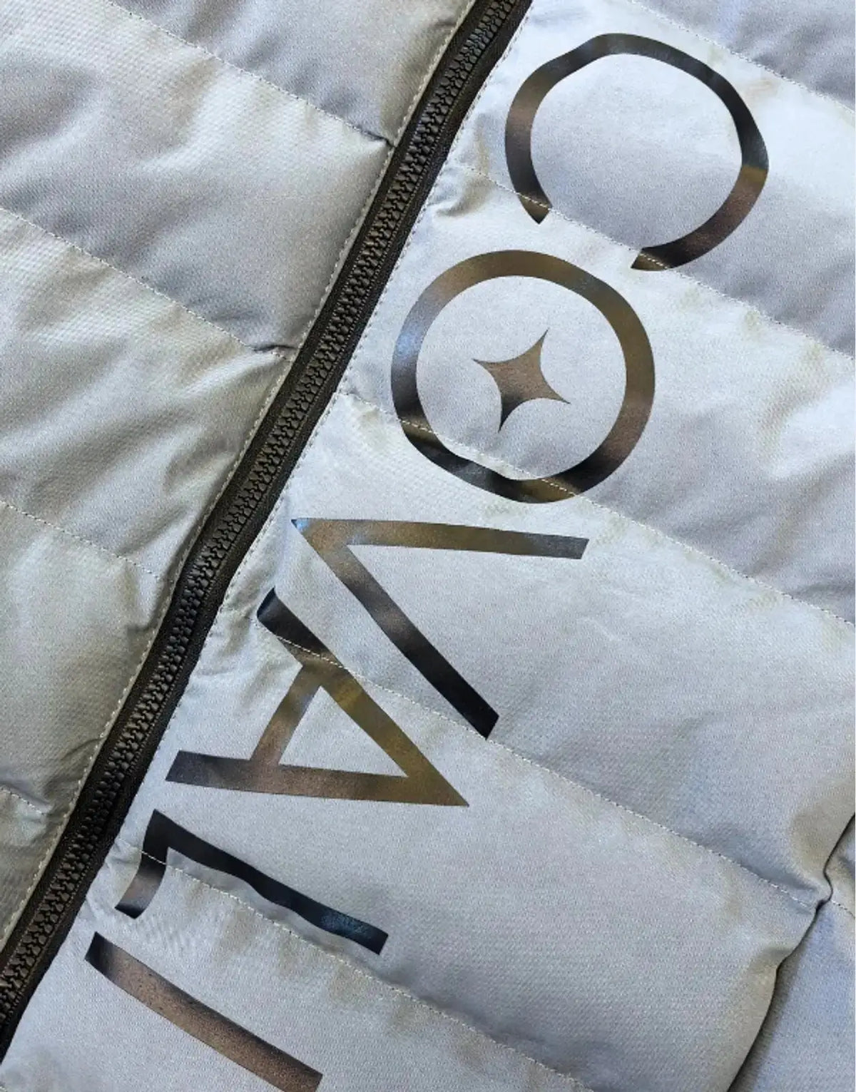 Close-up of a light grey Covali Inverno puffer jacket featuring visible quilting, a black zipper, and the Covali brand logo.