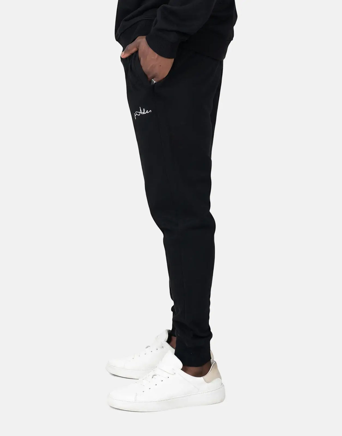 Black Fade Signature Sweatpants for men, featuring a white script logo on the thigh, worn with white sneakers.