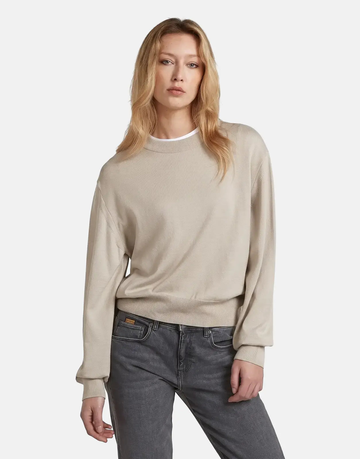 A woman models a G-Star RAW Boxy Knit Brick sweater in beige paired with dark gray jeans, captured from the waist up.