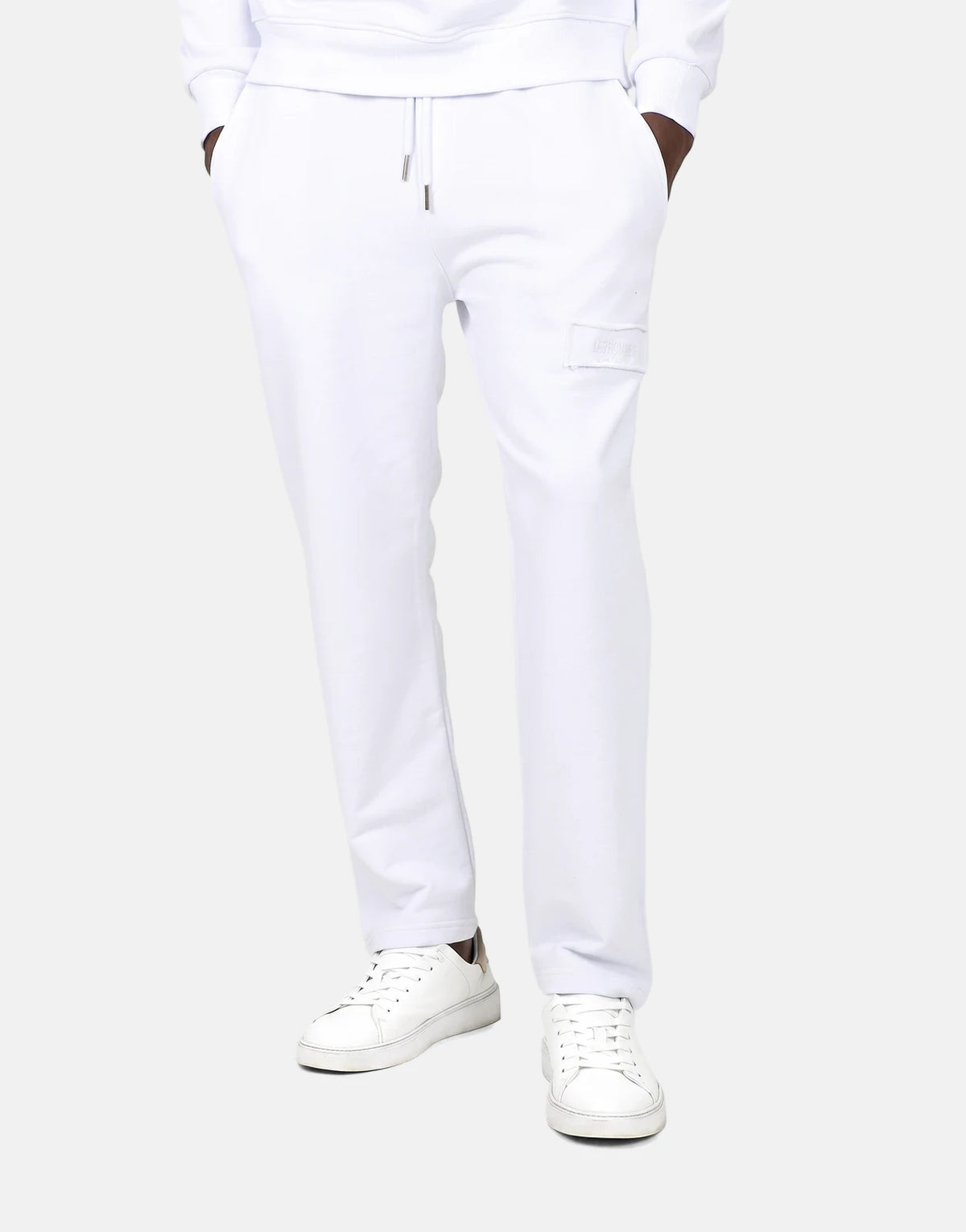Men's Les Hommes white jogger sweatpants, featuring a drawstring waist, side pockets, and a subtle patch logo on the thigh,