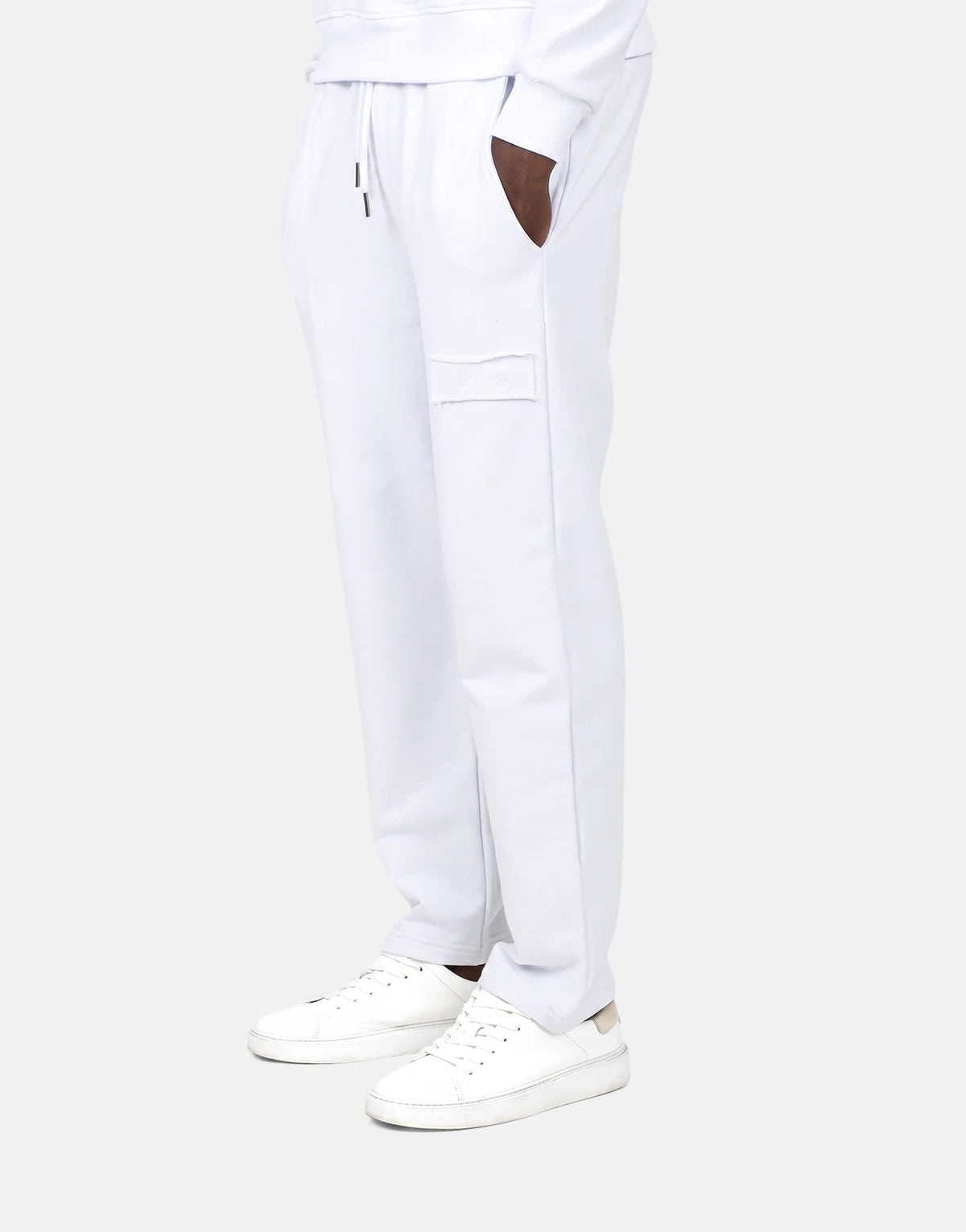 Men's Les Hommes white jogger sweatpants and white sneakers in a profile view, featuring a distressed patch and drawstrings.