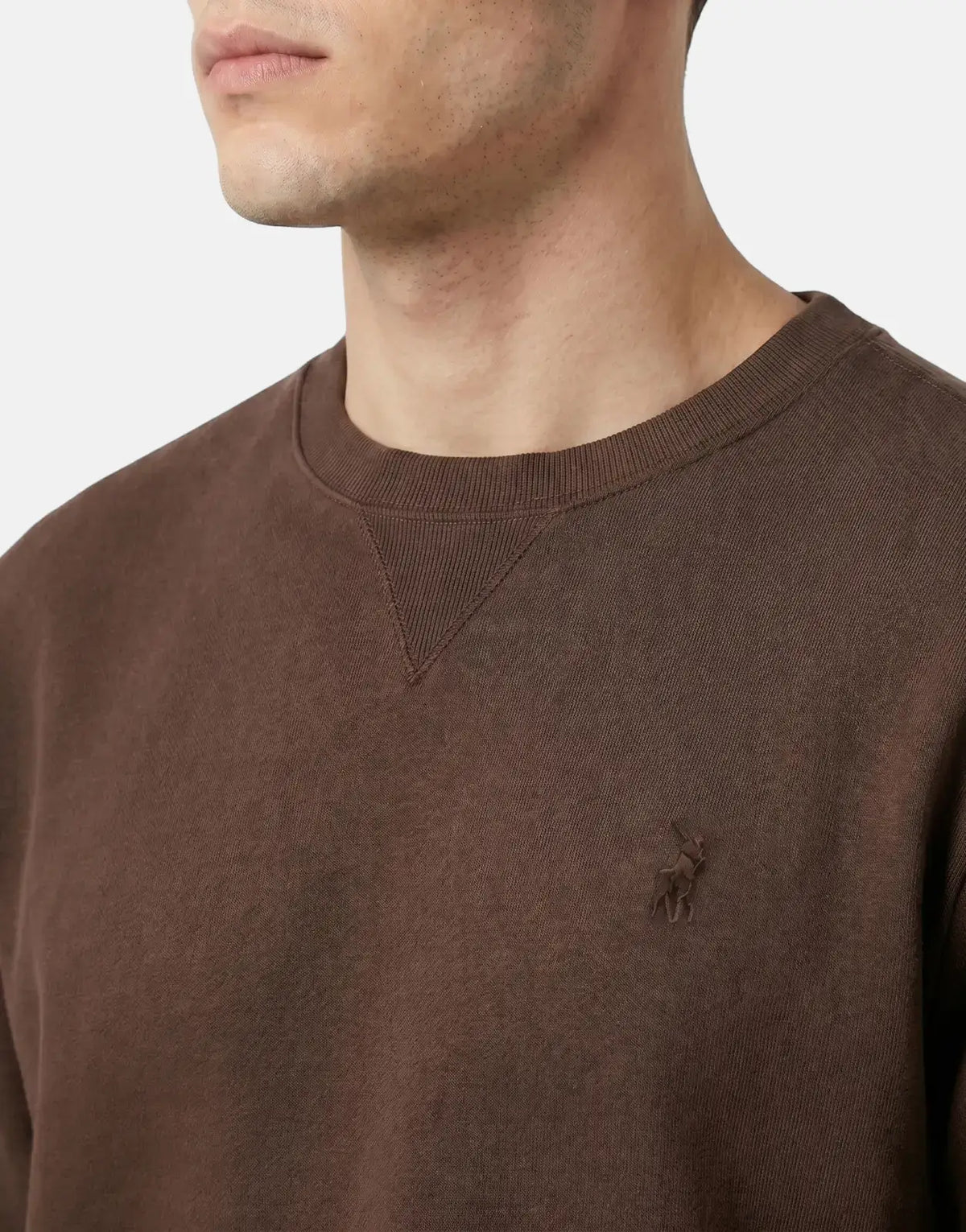 Close-up of a man wearing a brown Polo Essential Fleece Sweatshirt, showcasing the ribbed crew neck and embroidered logo.