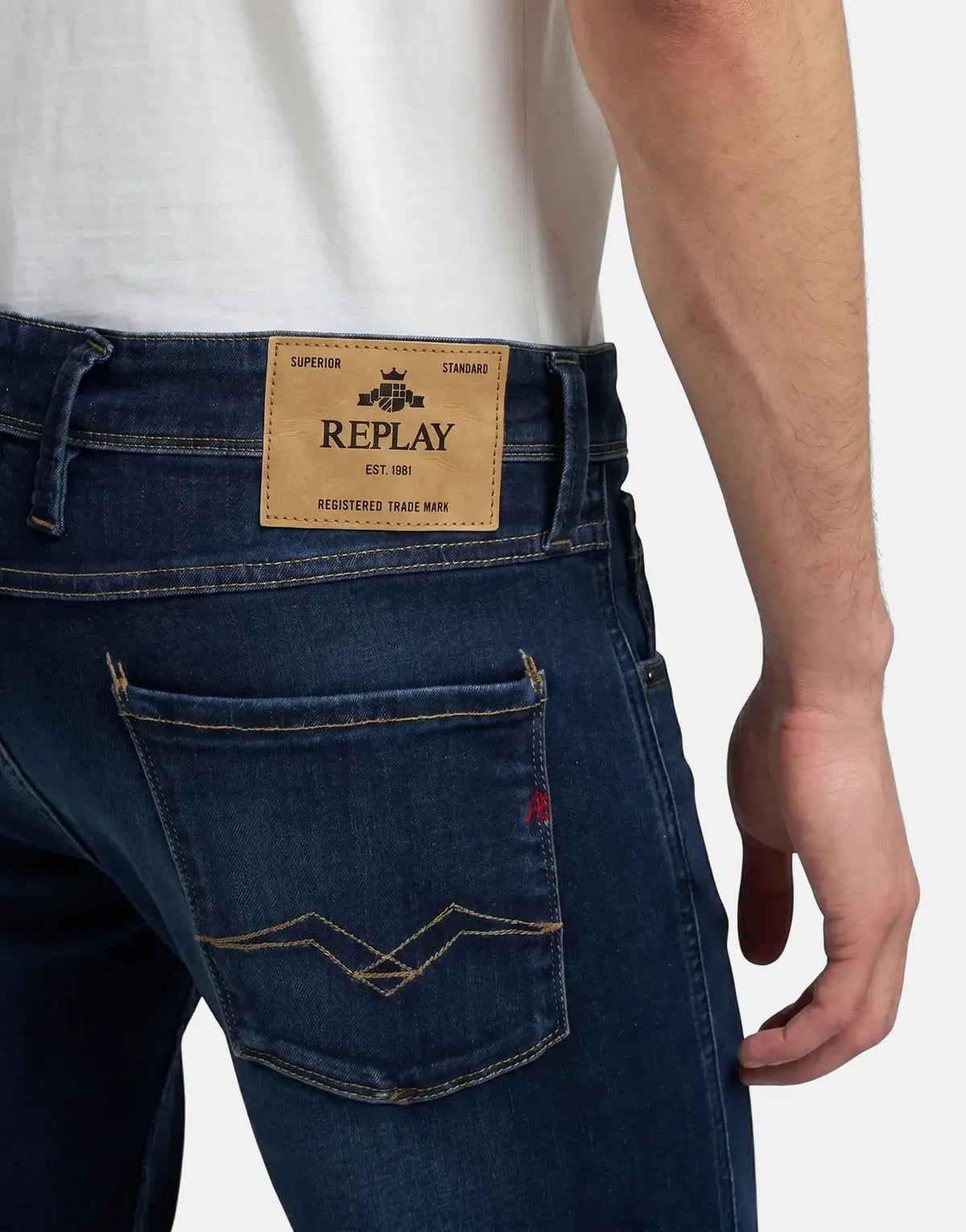 Close-up of a man wearing Replay Anbass dark blue jeans, highlighting the branded leather back label and detailed back