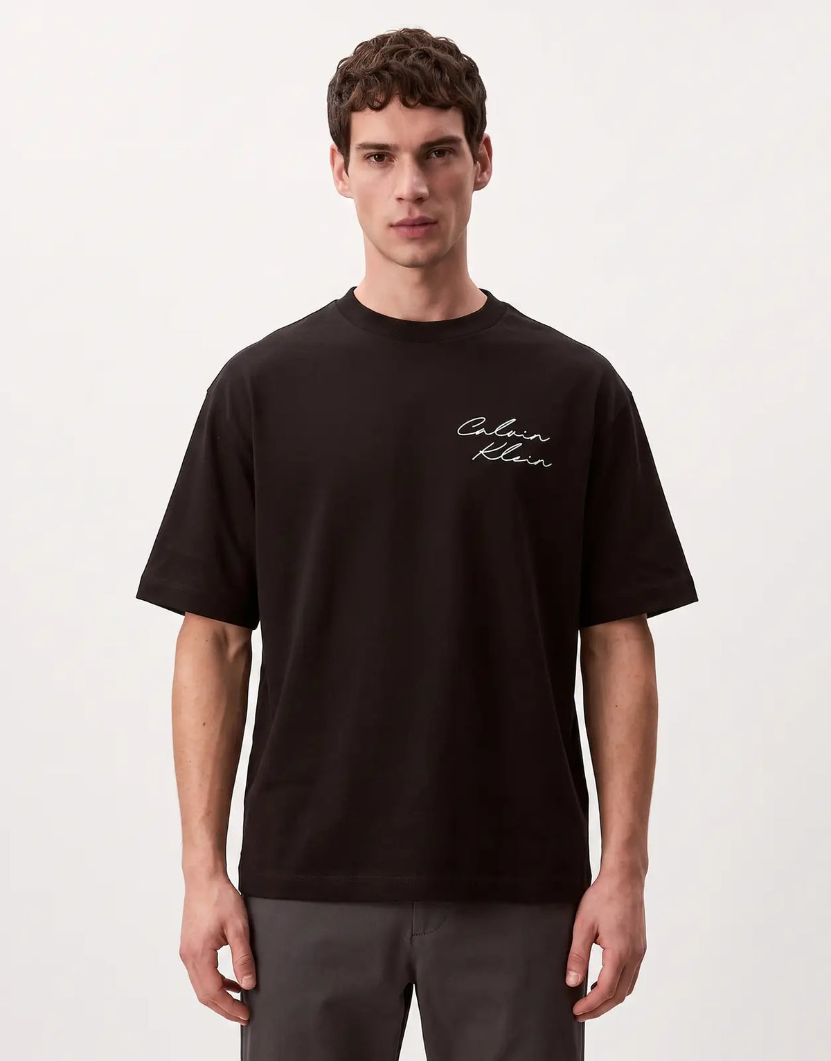 A Calvin Klein 16s April Graphic Seasonal Fashion t-shirt in black with a white script logo, worn by a male model.
