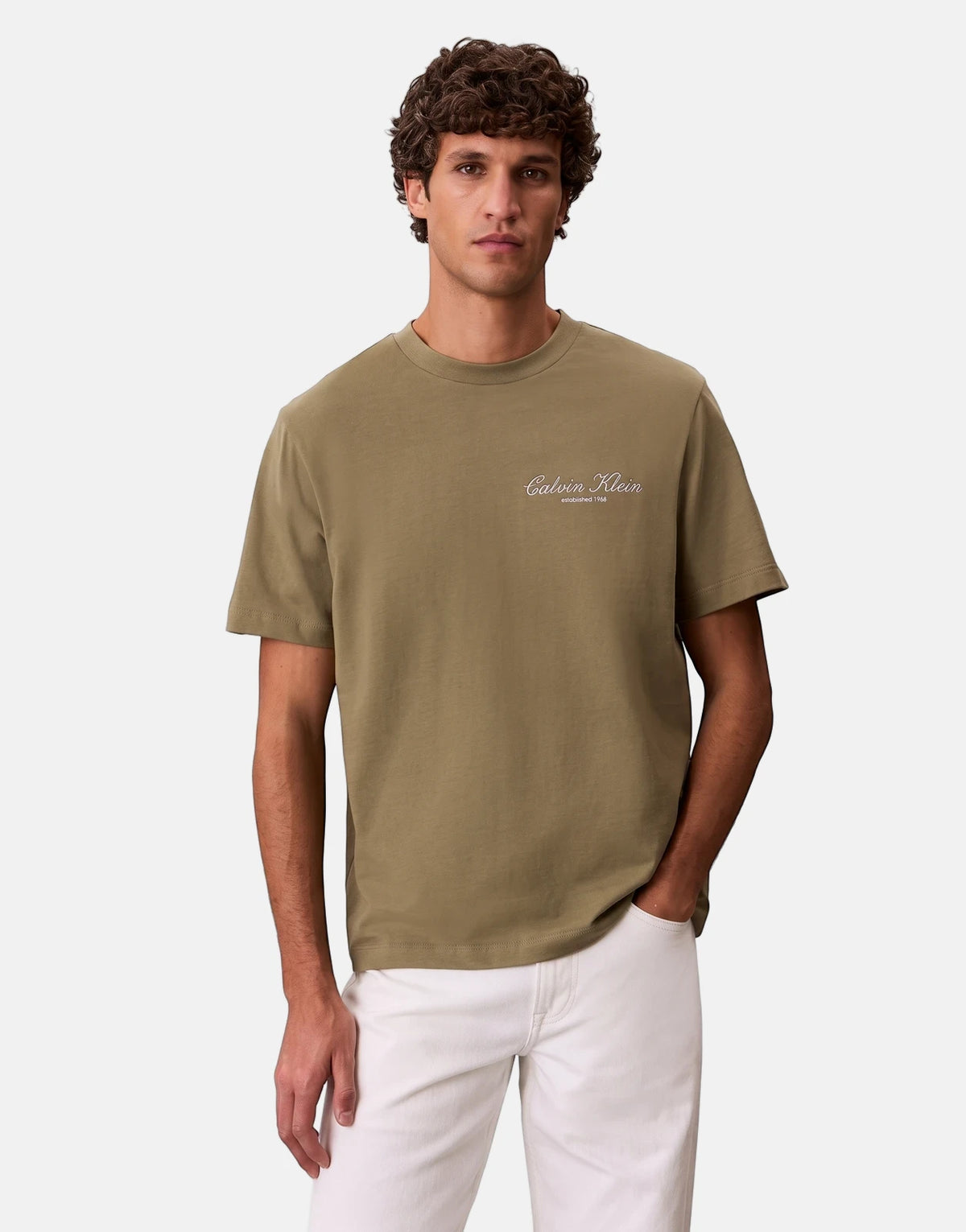 A male model wearing an olive green Calvin Klein 20s March Graphic Seasonal T-Shirt with white branding, paired with white