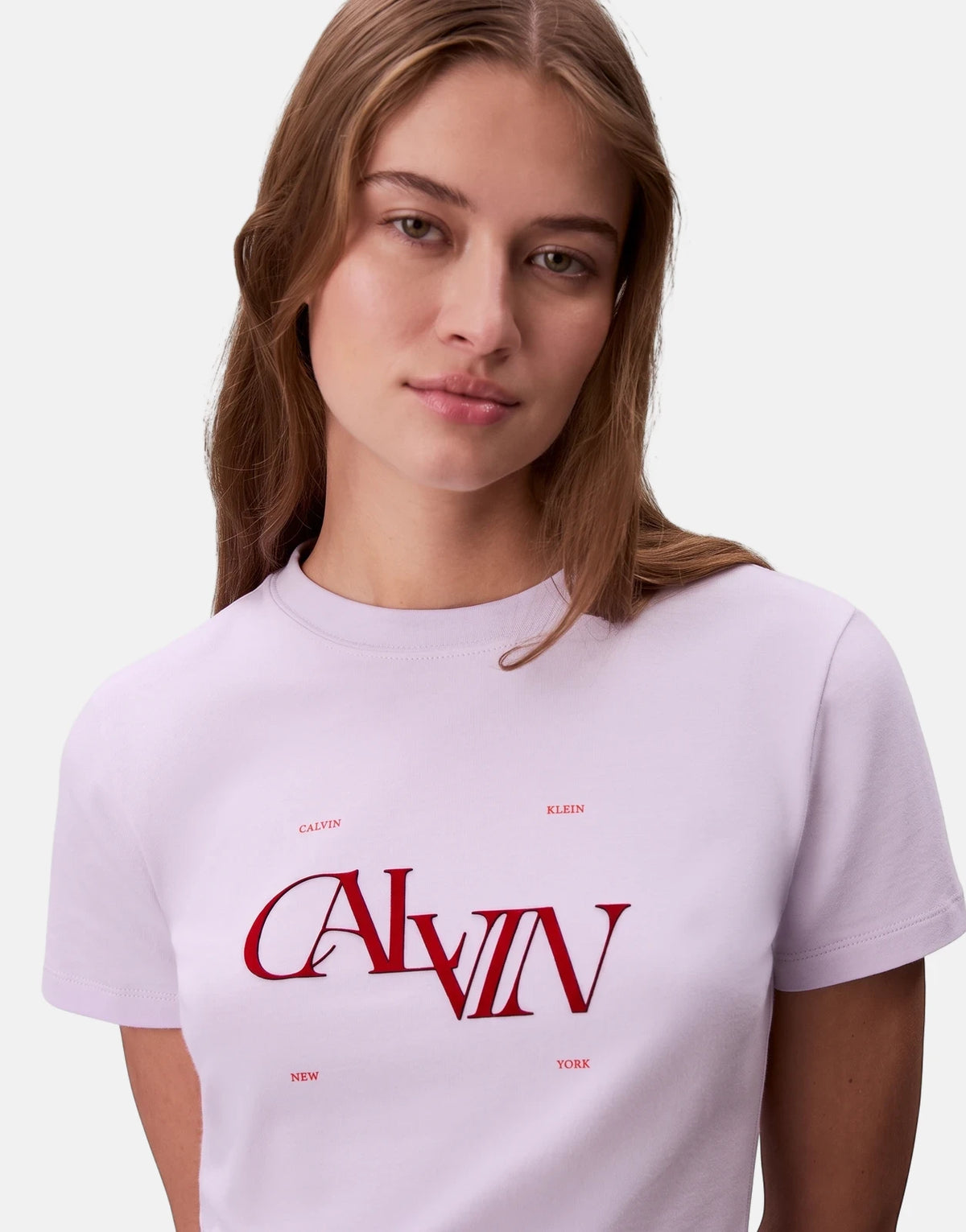 Female model wearing a Calvin Klein Seasonal Graphic Slim Lilac T-shirt with red branding print on a light background.