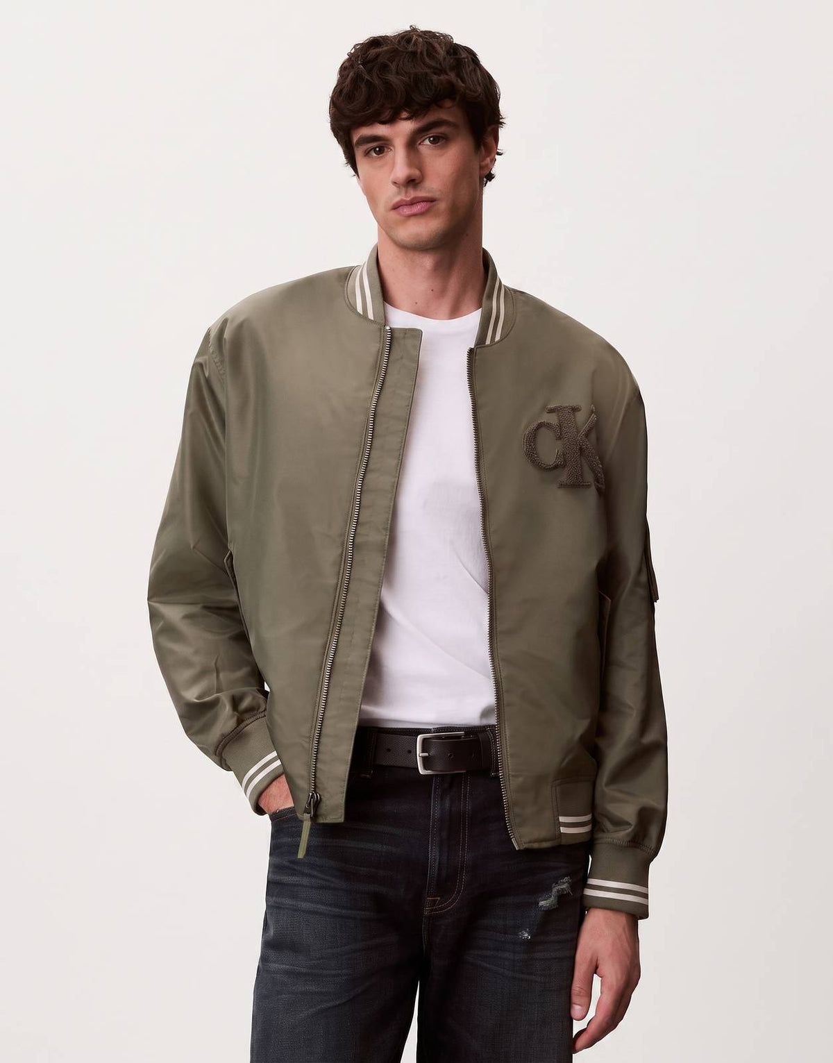 A male model wearing a Calvin Klein Tipped Hero Bomber Jacket in olive green, featuring a full-zip front and striped ribbed