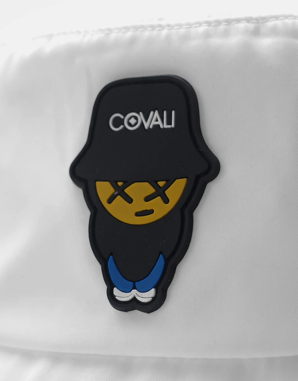 Covali Tipo White Bucket Hat, close-up view showing the brand's rubber logo patch with a character design.