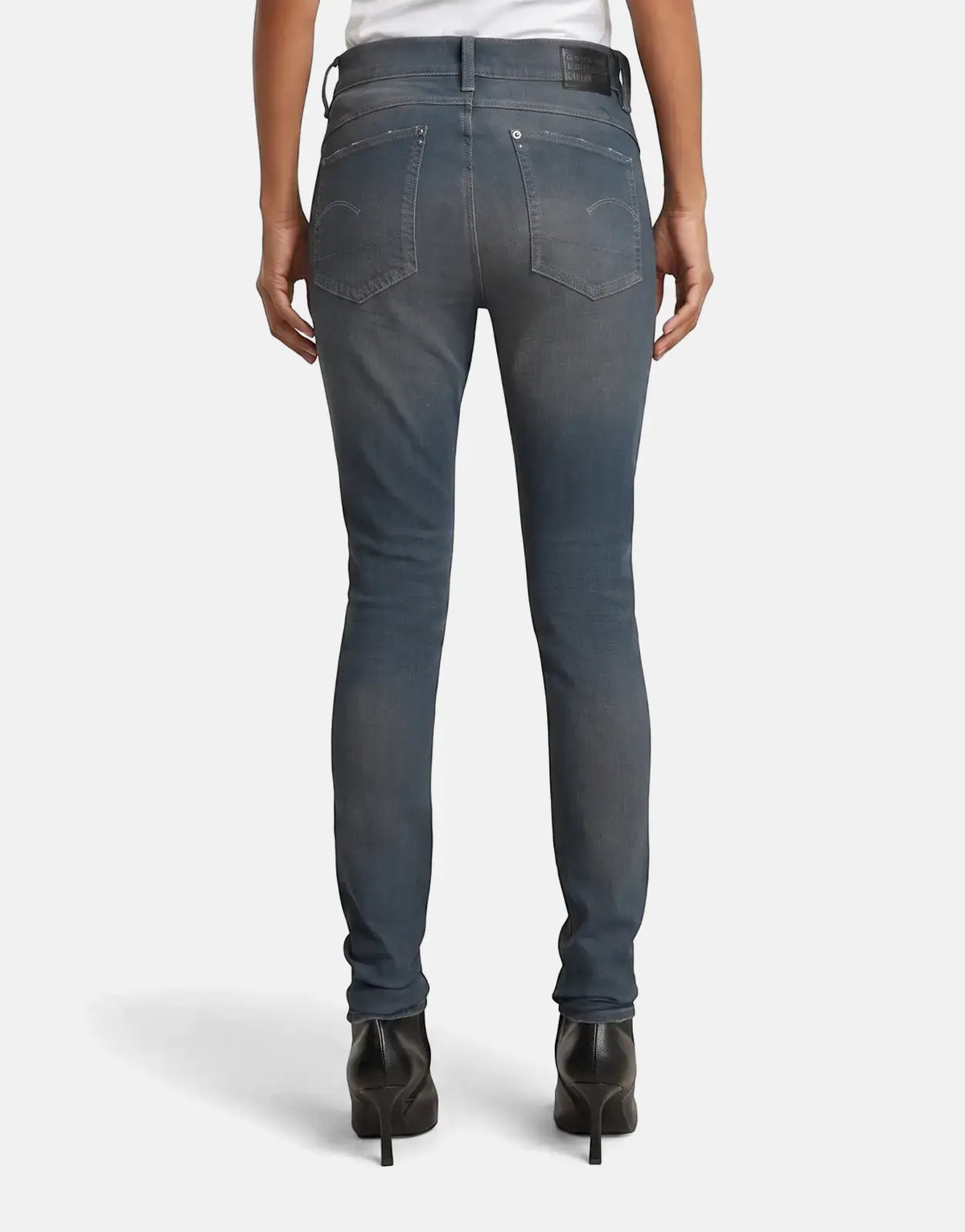 Rear view of a person wearing G-Star RAW Lhana skinny jeans in a worn-in smokey night blue wash with black high heels.