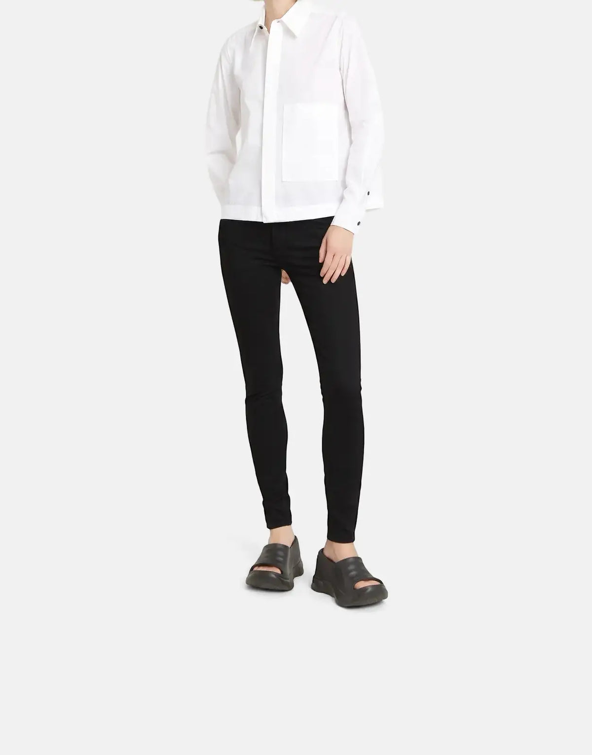 A blonde woman models G-Star RAW Lynn Mid Skinny Pitch Black Jeans, a white shirt, and black sandals on a light background.