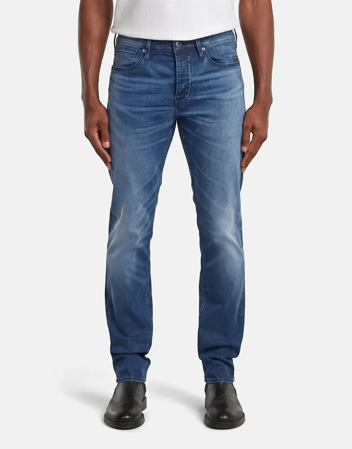 A man models G-Star RAW Streem Slim Tapered jeans in a worn medium blue wash, paired with black shoes, full length view.