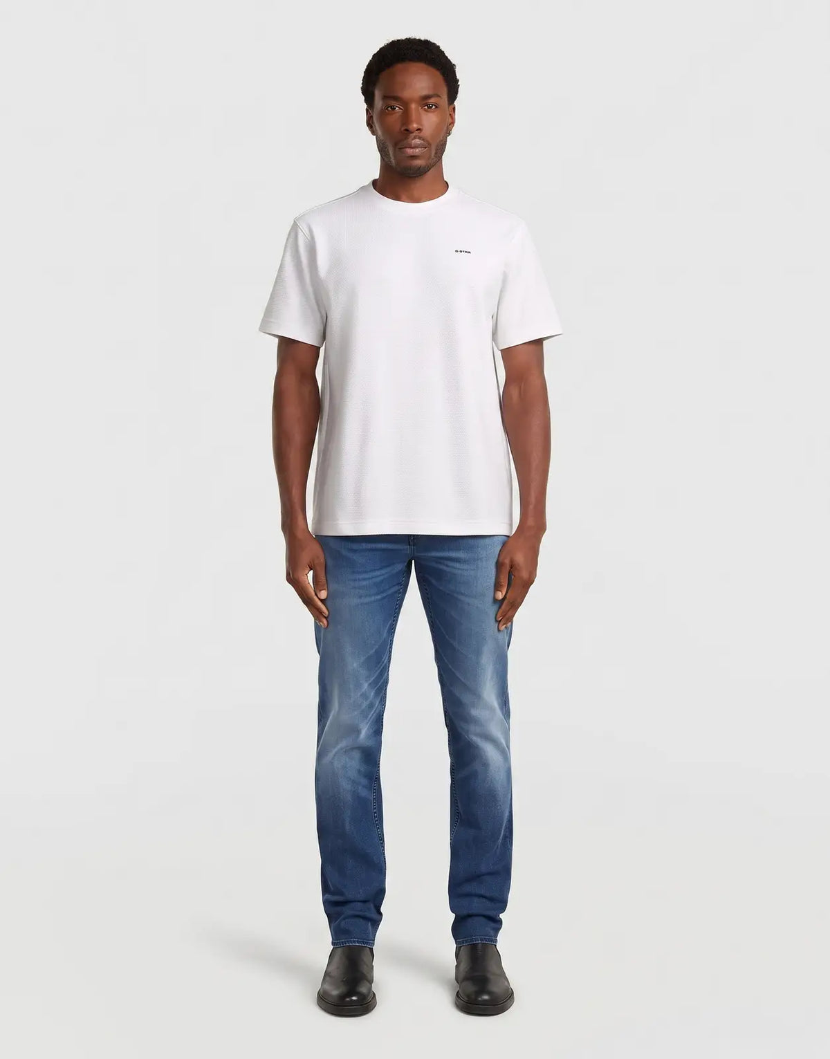 Front view of a male model wearing a G-Star RAW Streem Slim Tapered Worn in Diaz Beach white t-shirt, blue jeans, and black
