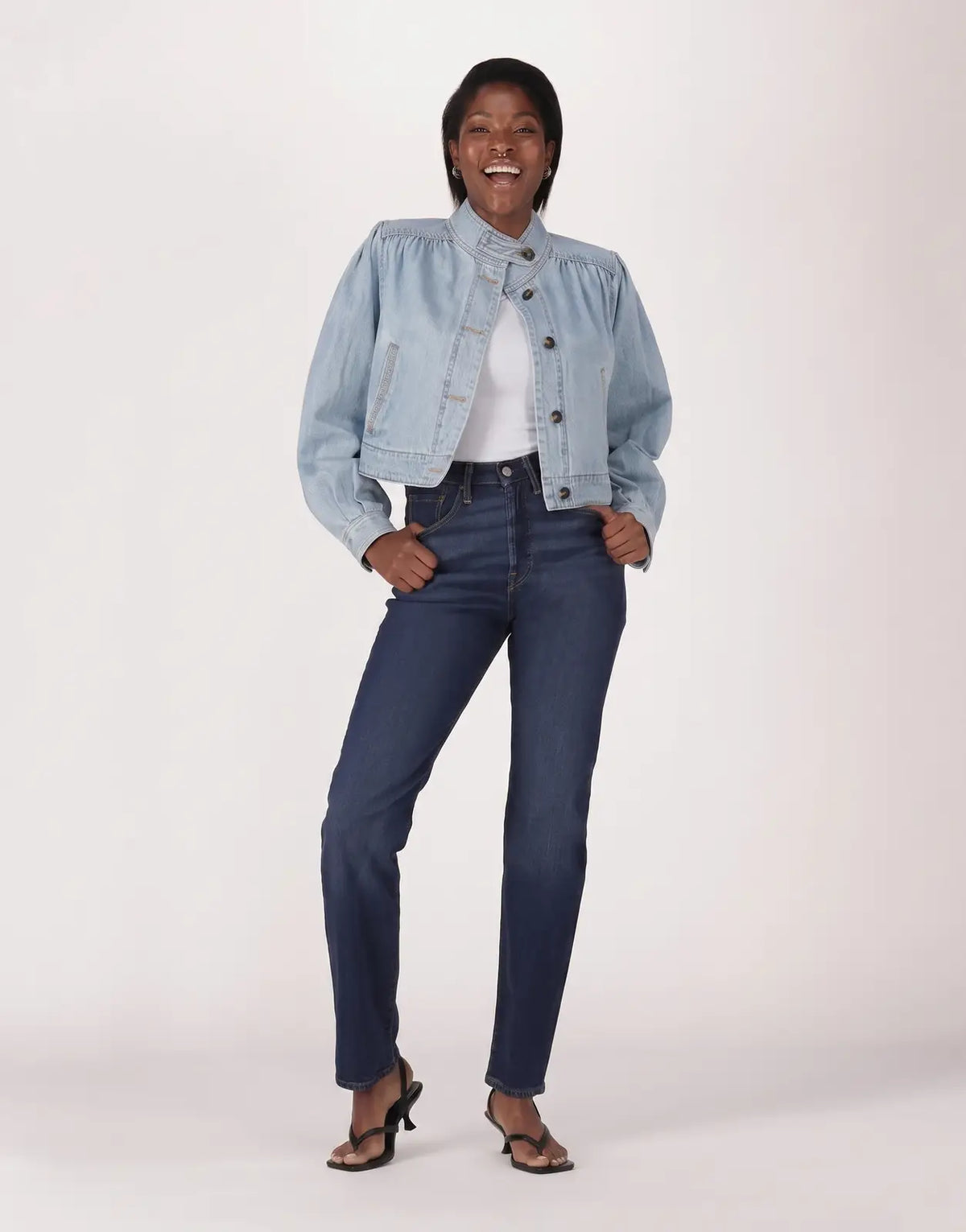 A smiling model wears Levis 501 Ladies Time Take Jeans in dark blue with a light wash denim jacket, full body shot.