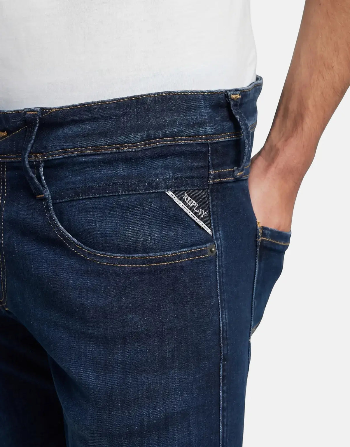 Close-up of Replay Anbass dark blue denim jeans, featuring the back label on the coin pocket and a hand in the front pocket.